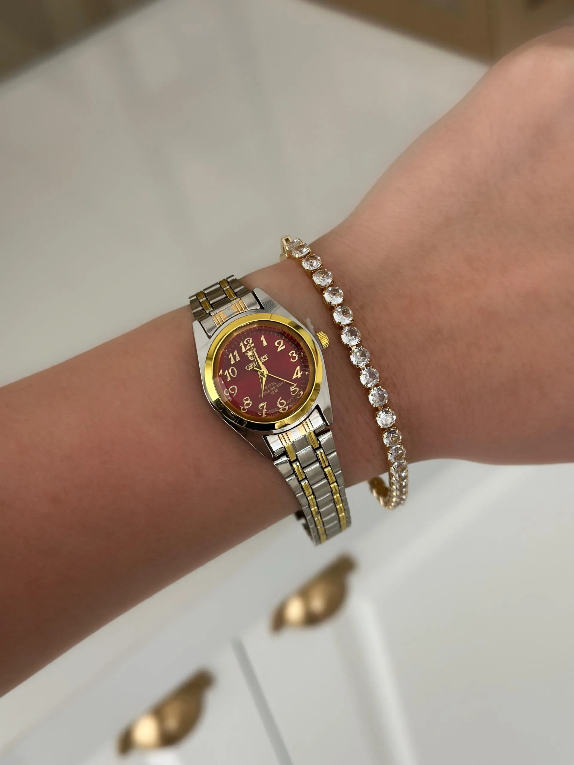 Relógio Prateado com Listras Douradas com Fundo Vermelho